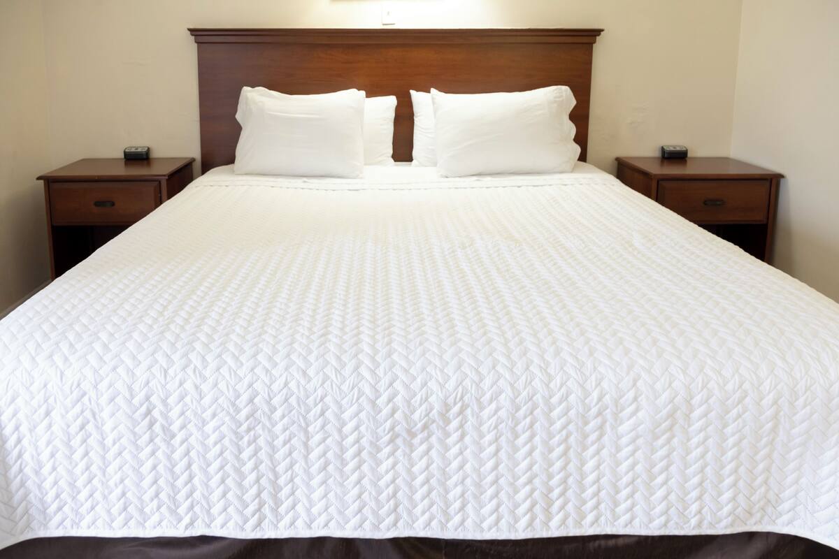 A neatly made bed with a white quilt, two wooden nightstands, and a wooden headboard.