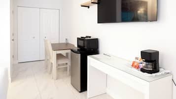 Una cocina compacta con microondas, refrigerador y cafetera sobre una mesa de vidrio.