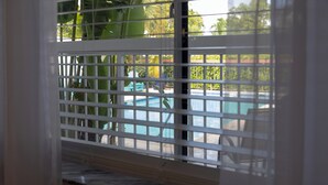 A window with blinds partially covering a view of a swimming pool and outdoor furniture.