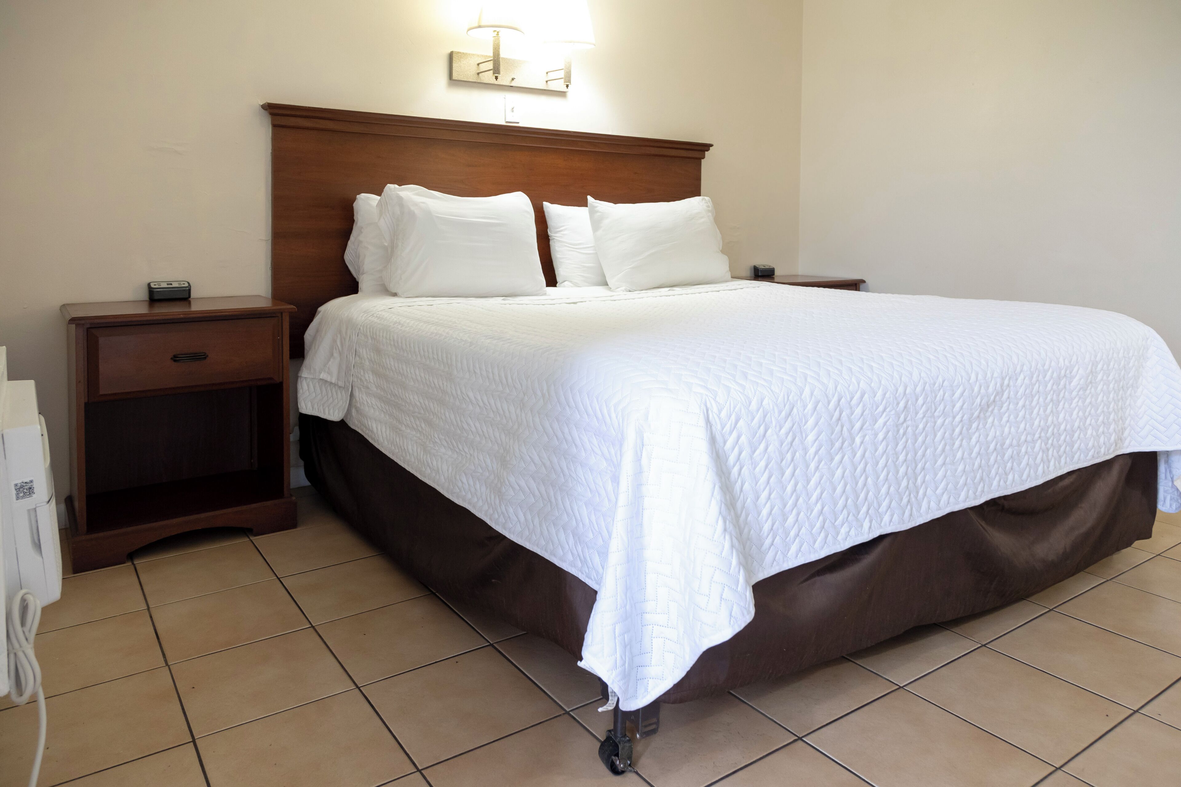 A hotel room with a large bed, wooden headboard, bedside tables, and a wall-mounted light fixture.