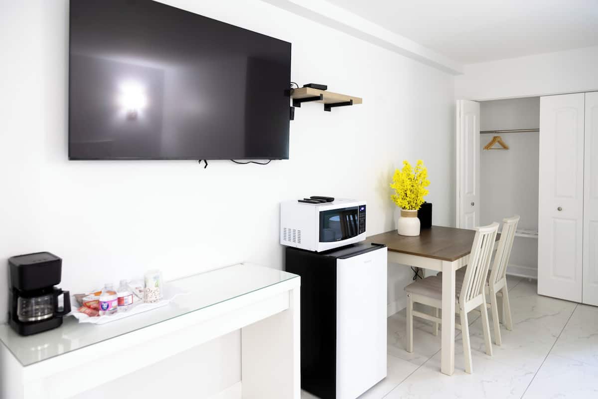 A modern kitchen with a flat-screen TV, a coffee maker, a microwave, and a dining area with chairs.