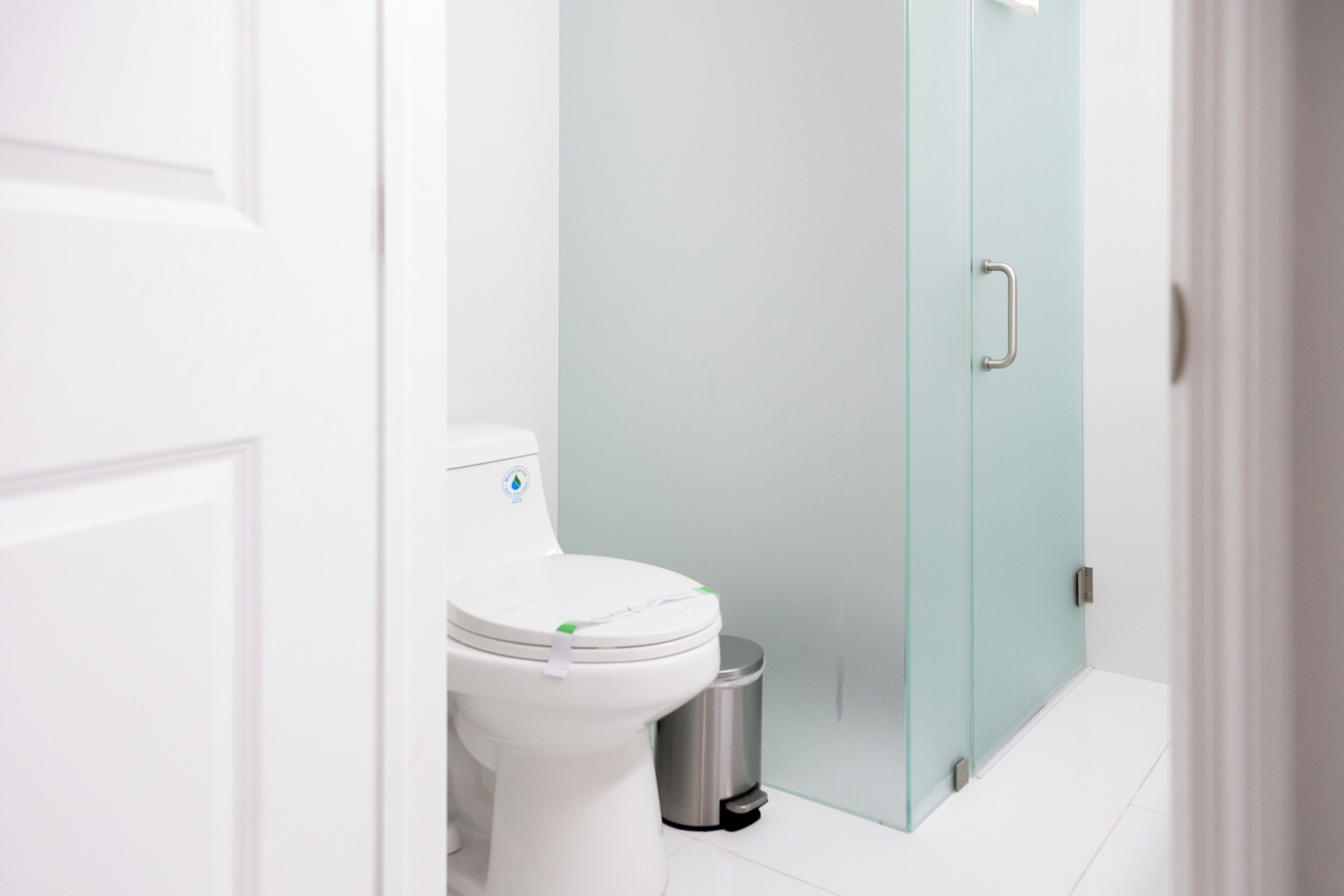A modern bathroom with a white toilet, a trash bin, and a frosted glass door.