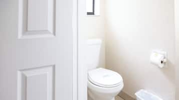 A white door leading to a bathroom with a toilet, a trash bin, and a toilet paper holder on the wall.