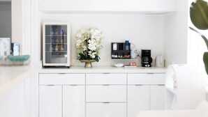 A modern kitchen with white cabinets, a refrigerator, a coffee maker, and a flower vase.