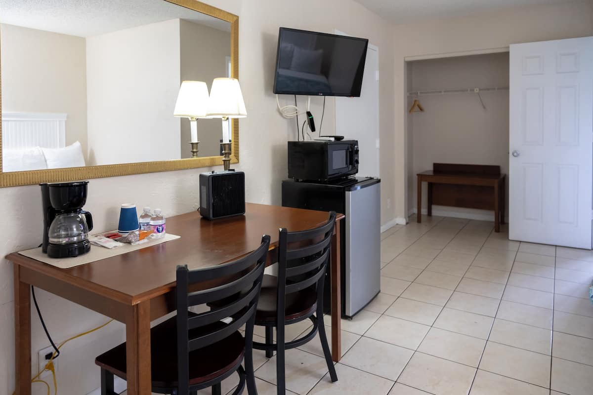 A hotel room with a dining table, chairs, a microwave, a television, a lamp, and a coat rack.