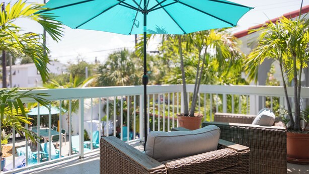 A balcony with wicker furniture, a turquoise umbrella, and potted plants.