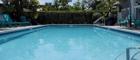 A swimming pool with clear blue water, surrounded by green lounge chairs and palm trees.