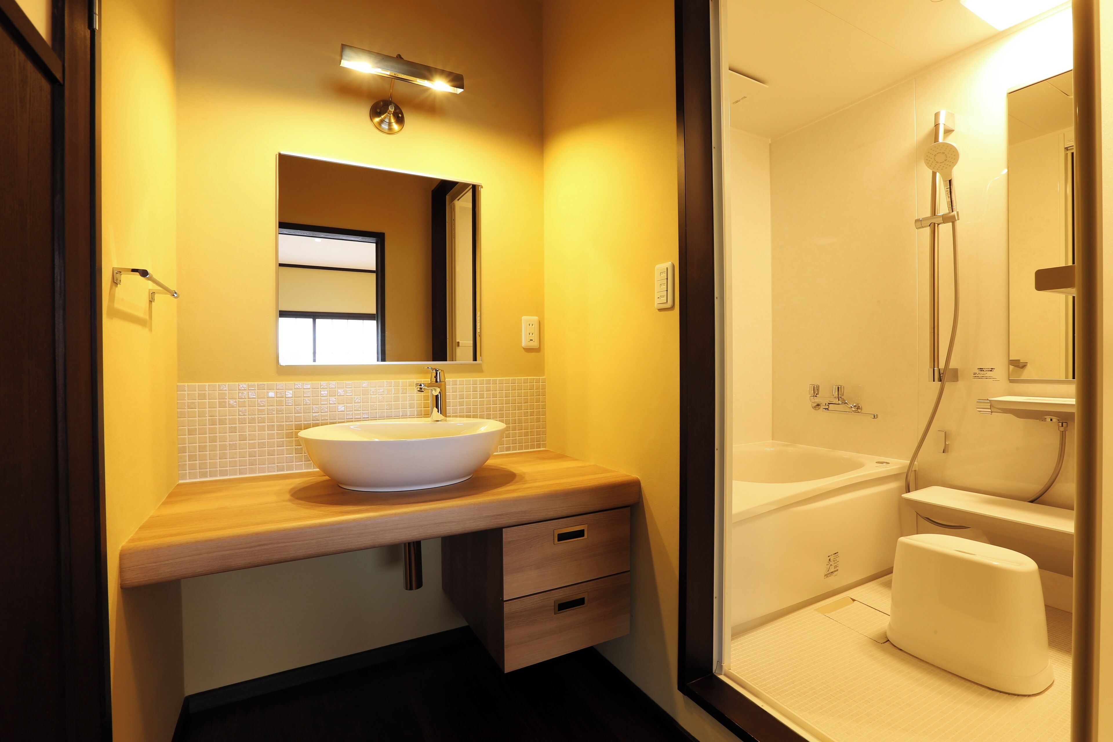 A modern bathroom with a wooden vanity, a large mirror, a white sink, a bathtub, and a shower area.