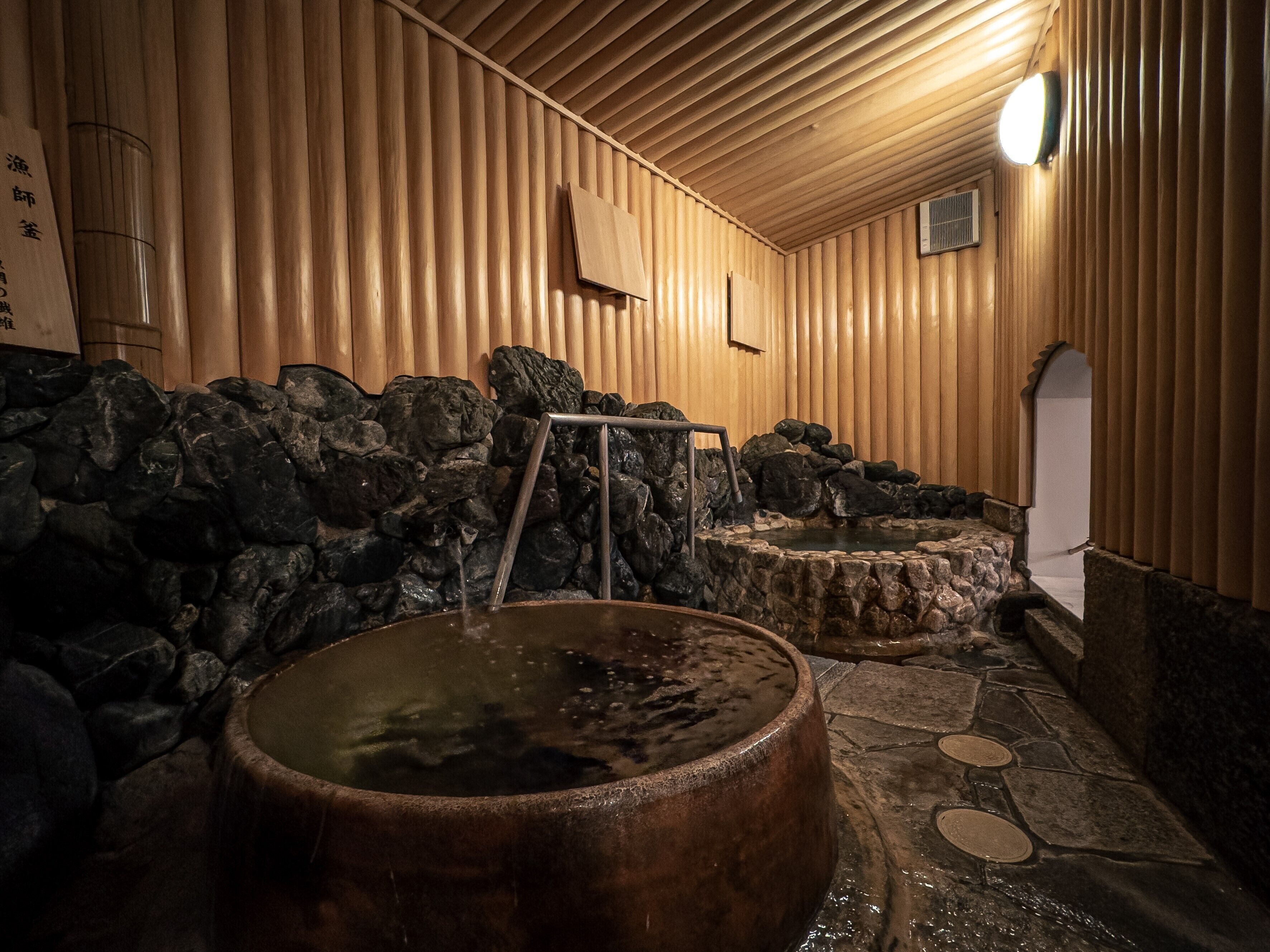 A traditional Japanese onsen with wooden walls, stone steps, and a wooden hot spring tub.