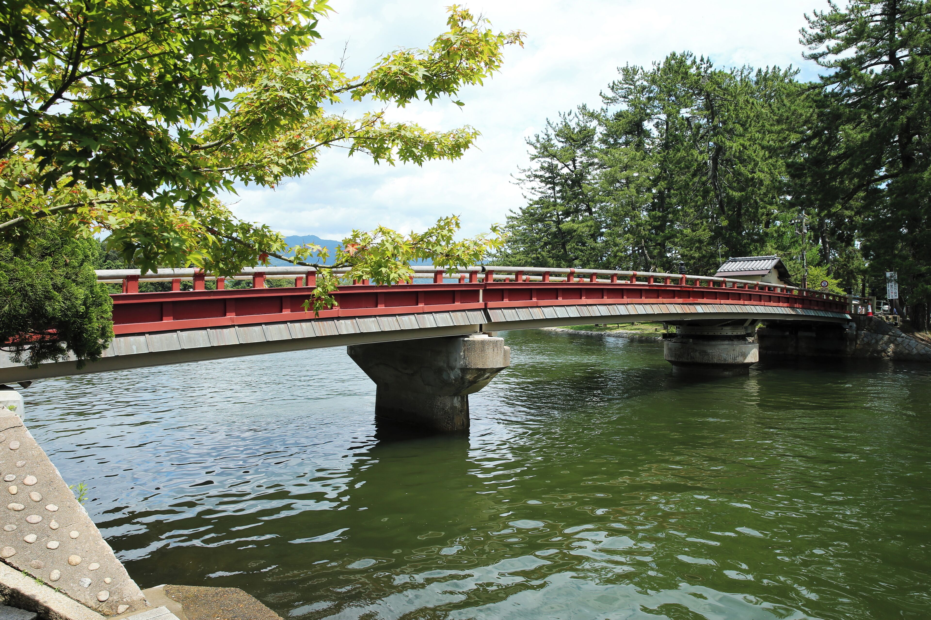 A bridge over a body of water, surrounded by trees and a clear sky.