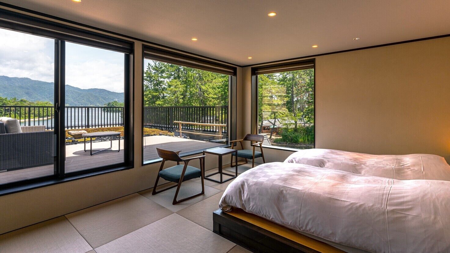 A bedroom with a large bed, a desk, and a chair, with a balcony and a view of mountains.