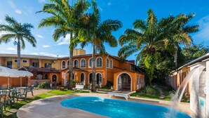 A pool area with a water feature, outdoor seating, and a building with arched windows. - Vale Verde Praia Hotel (Porto Seguro)