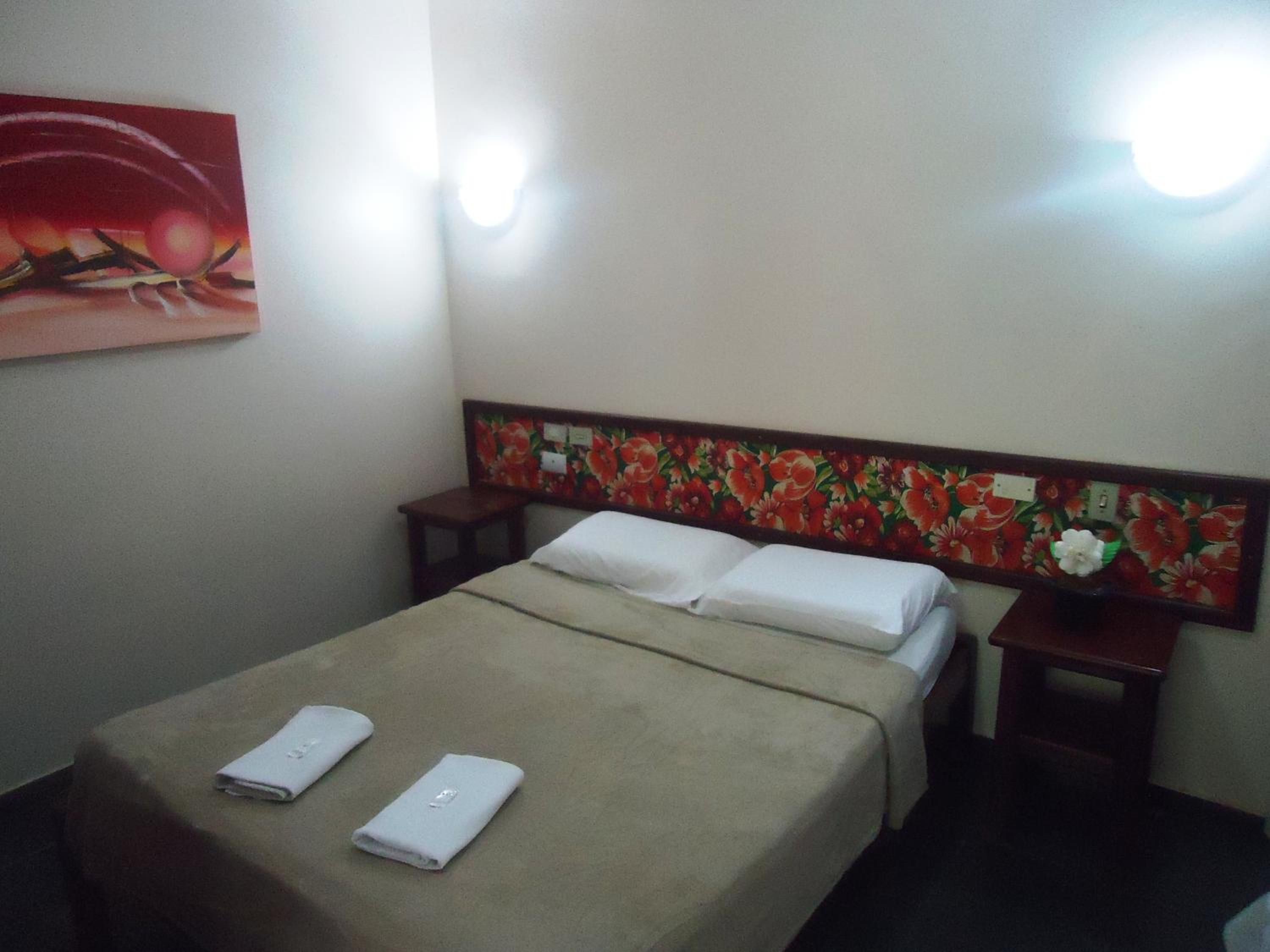 Habitació d'hotel amb un llit, una petita taula de nit, un televisor fixat a la paret i un quadre.