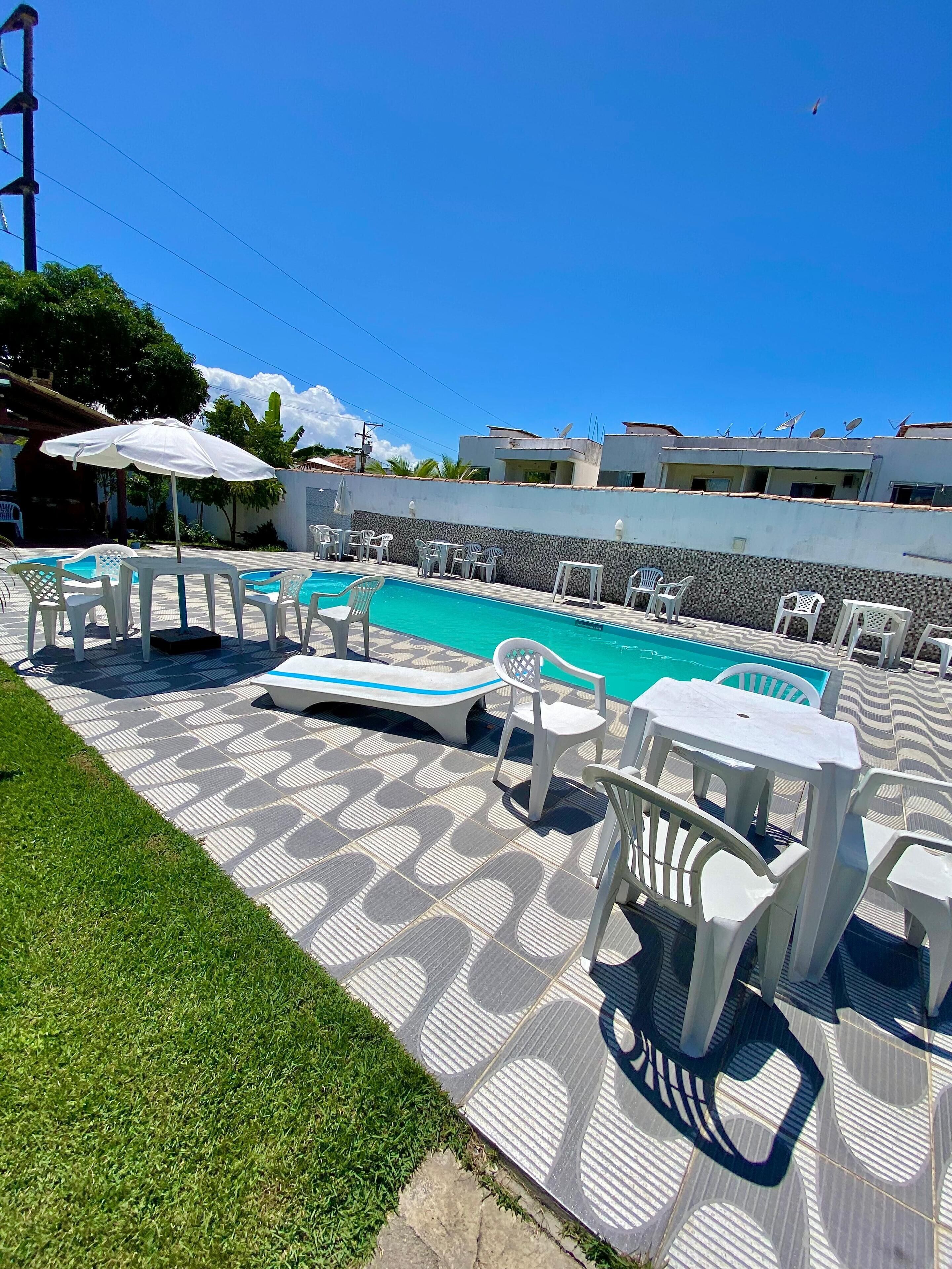 A swimming pool area with white plastic chairs and tables, surrounded by a patterned patio.
