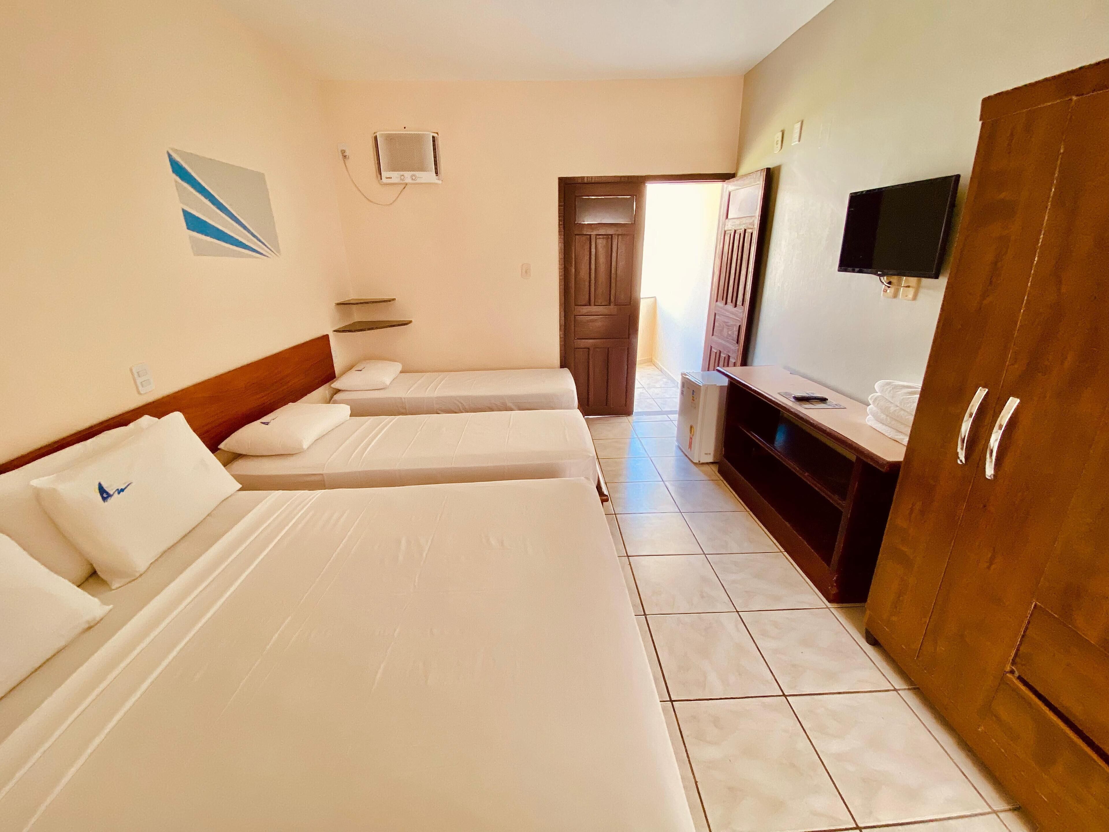 A hotel room with three single beds, a wooden wardrobe, a television, and a small refrigerator.
