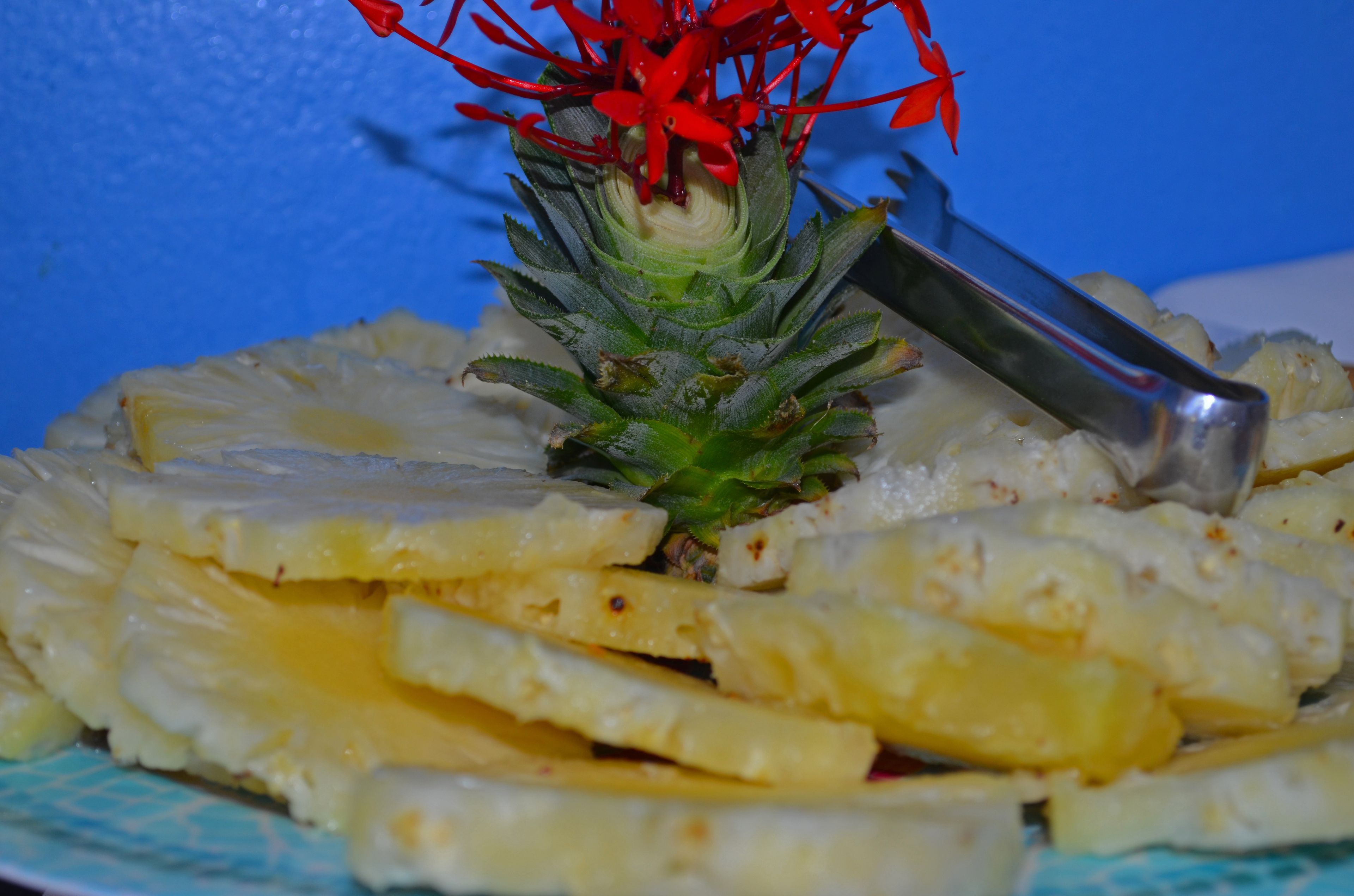 A plate of sliced pineapple with a decorative red flower on top.