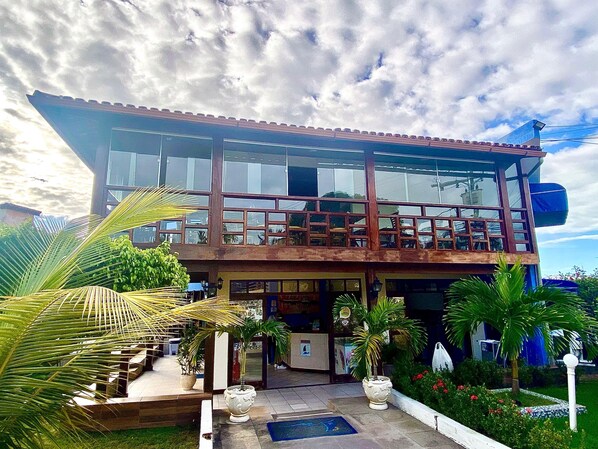 A two-story building with large windows, a balcony, and a well-maintained garden with palm trees and flowers. - Hotel Porto das Âncoras (Porto Seguro)