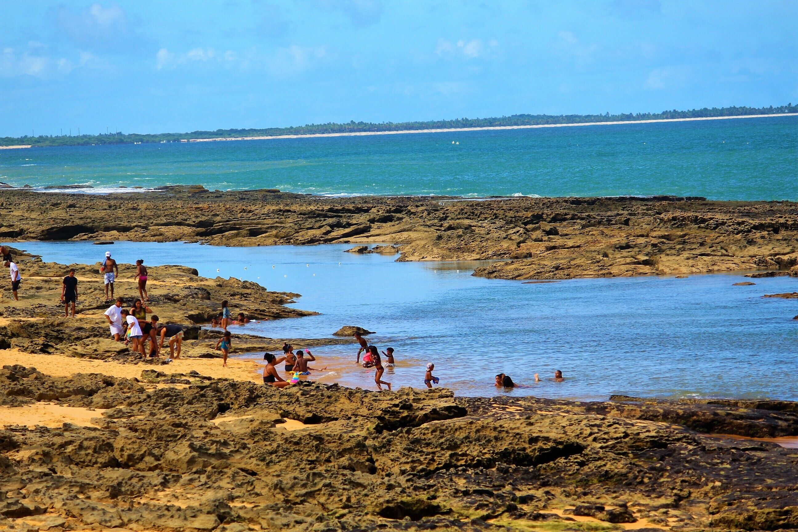 Una playa rocosa con gente nadando y caminando por la orilla.