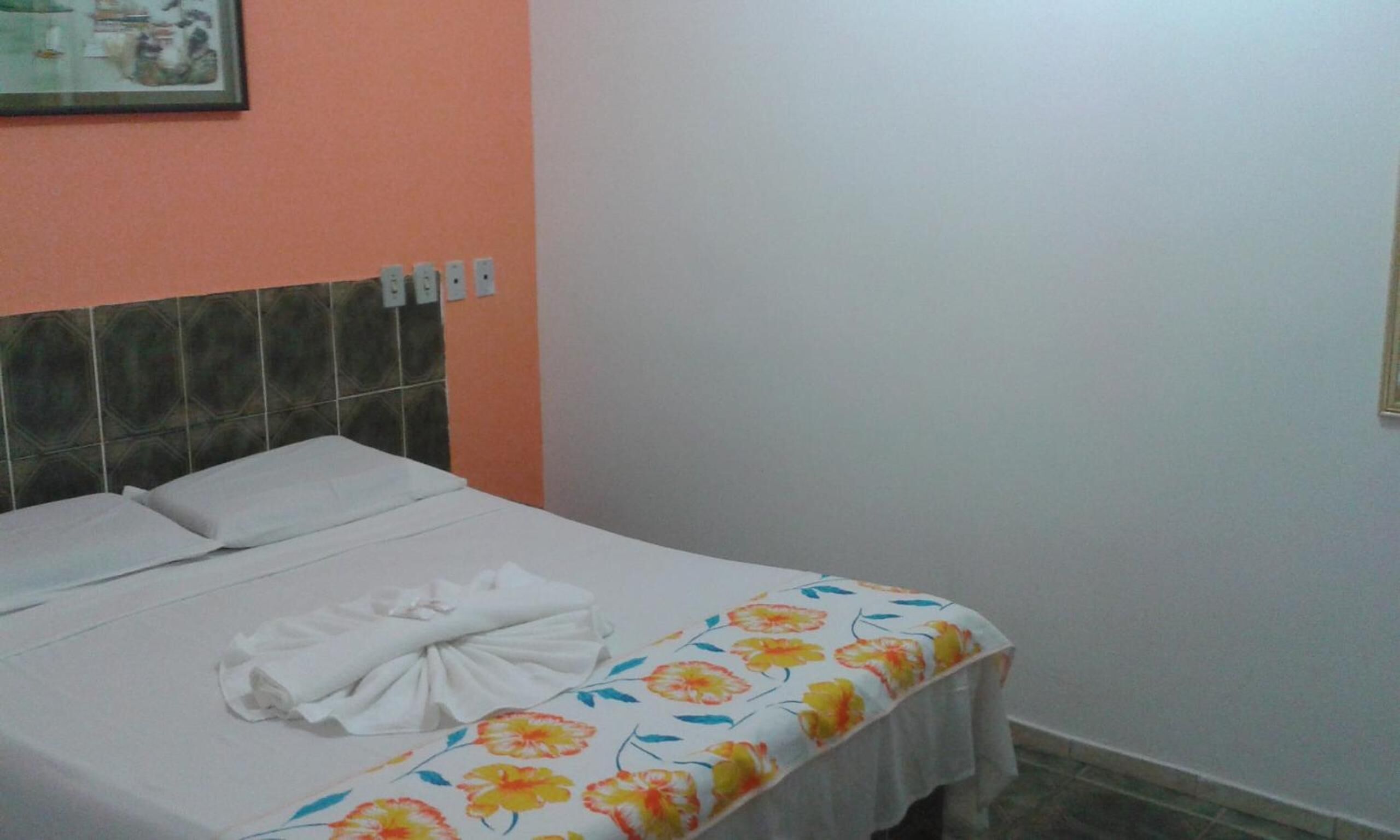 Een eenpersoonsbed met een bloemenprint sprei en witte kussens in een kamer met oranje wanden en een betegeld hoofdeinde.