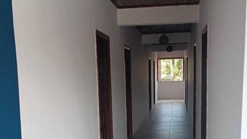 Um corredor comprido e estreito, com paredes brancas e chão de azulejos.