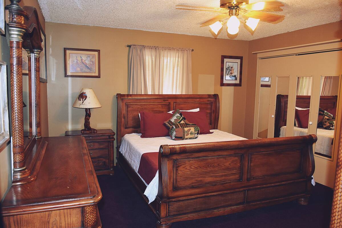 A wooden four-poster bed with a red throw pillow, a nightstand with a lamp, and a ceiling fan.