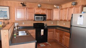 A kitchen with wooden cabinets, a stainless steel sink, a microwave, a refrigerator, and a small island with a sink. - Yellowstone River Suites (Gardiner)