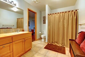 A bathroom with a wooden vanity, a mirror, a toilet, and a shower curtain. - Yellowstone River Suites (Gardiner)