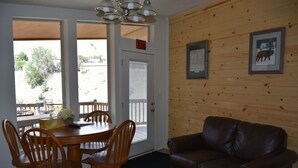 A dining area with a wooden table and chairs, a brown leather couch, and a view through a door. - Yellowstone River Suites (Gardiner)