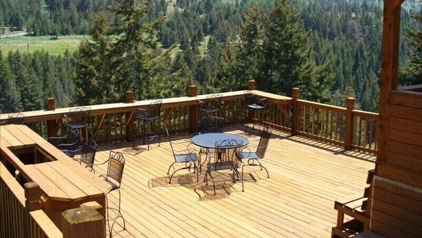 Una terraza de madera con mobiliario exterior y vistas a un valle boscoso.