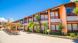 A hotel with a covered outdoor seating area, multiple windows, and palm trees. - Monte Pascoal Praia Hotel (Porto Seguro)