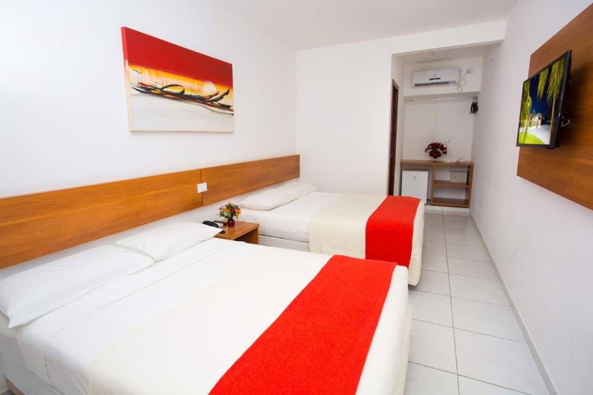 A hotel room with two beds, a TV, and artwork on the walls.