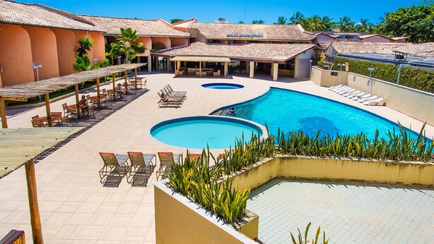A hotel with a large pool, outdoor seating, and a covered patio area. - Monte Pascoal Praia Hotel (Porto Seguro)