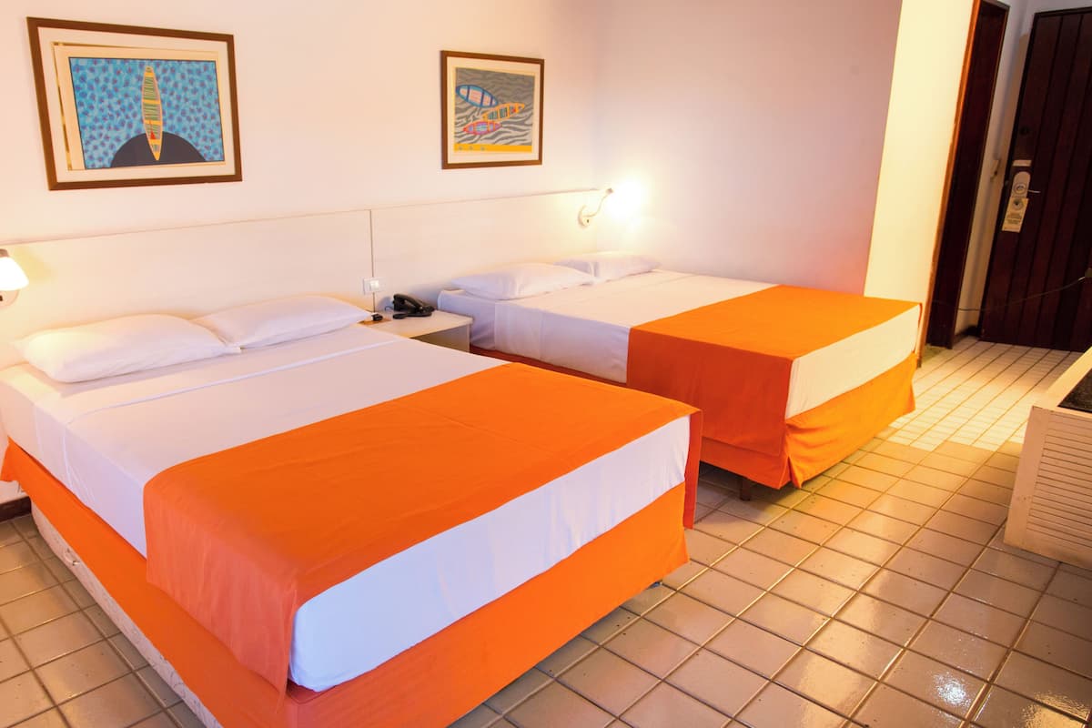A hotel room with two beds, white bedding, orange bedspreads, a nightstand with a phone, and two framed pictures on the wall.