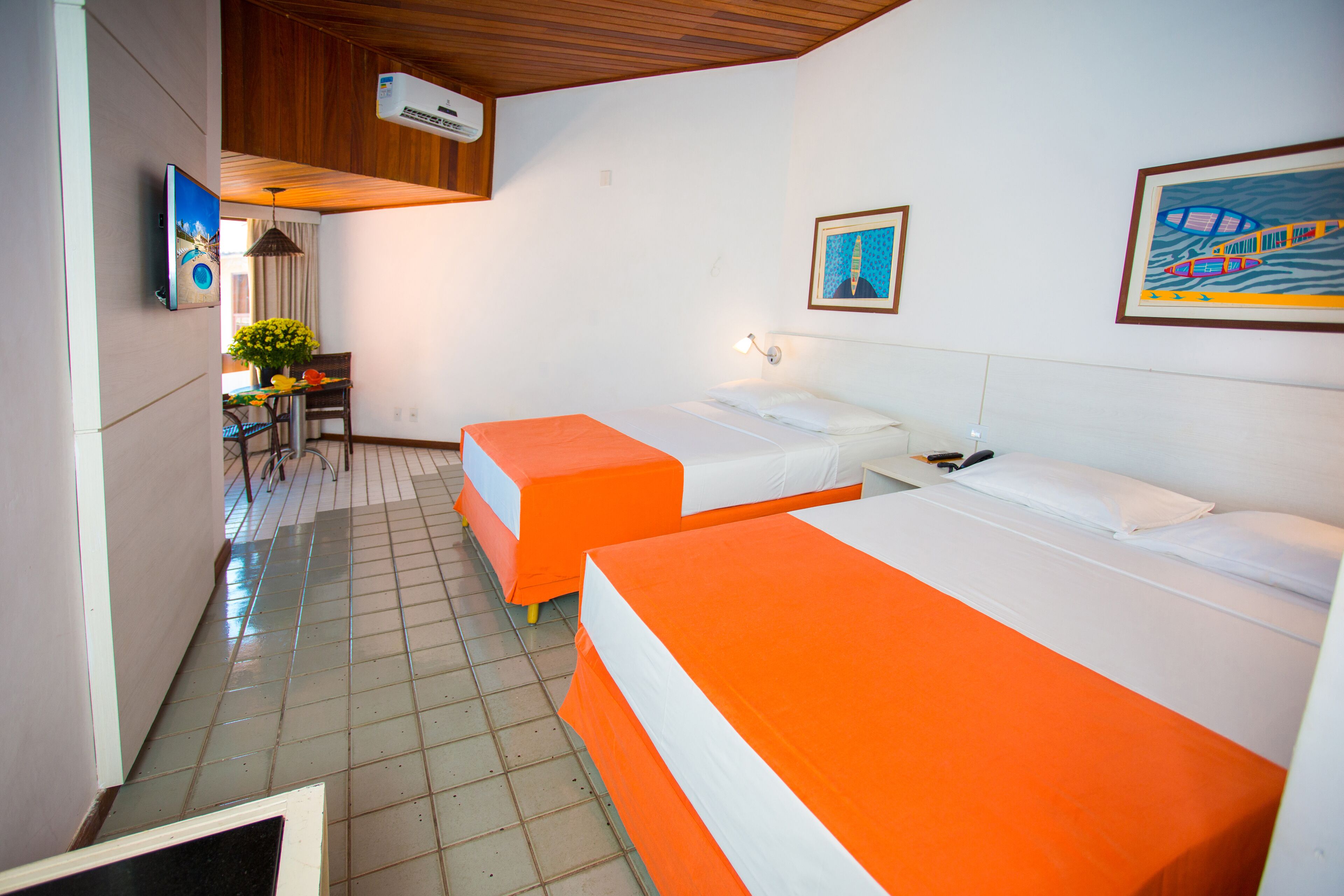 A hotel room with two beds, a desk, a chair, and a small table with a plant.