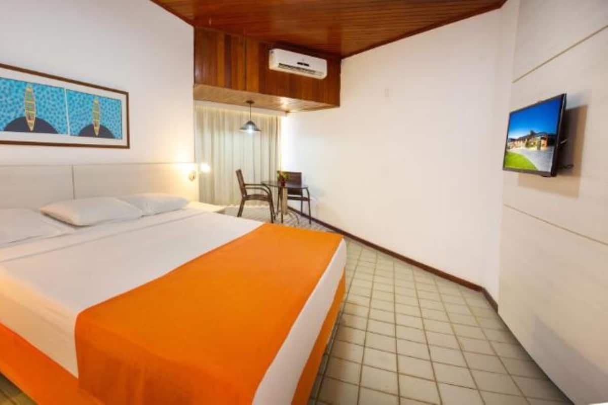A hotel room with a bed, a bedside table with a phone, a framed picture on the wall, and a television mounted on the wall.
