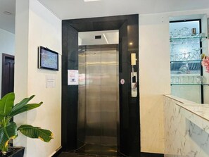 Un ascensor con pantalla digital, un letrero de prohibido fumar y una vitrina de vidrio con objetos a la derecha.