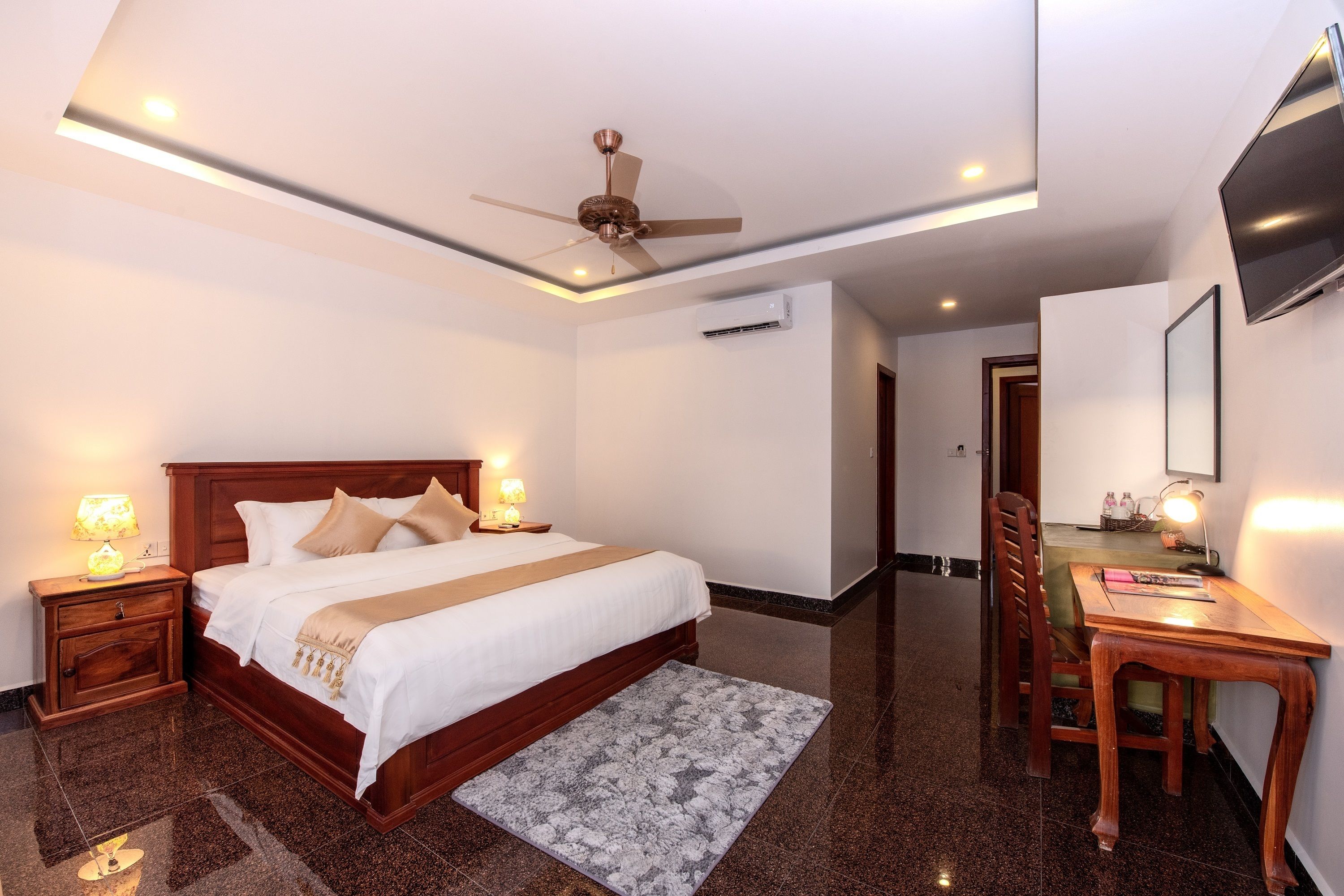 Habitación de hotel con cama, mesitas de noche, escritorio, silla, ventilador de techo y televisor.
