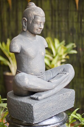 Una estatua de piedra de una figura sentada con un diseño sencillo y sin adornos, ubicada sobre un pedestal.