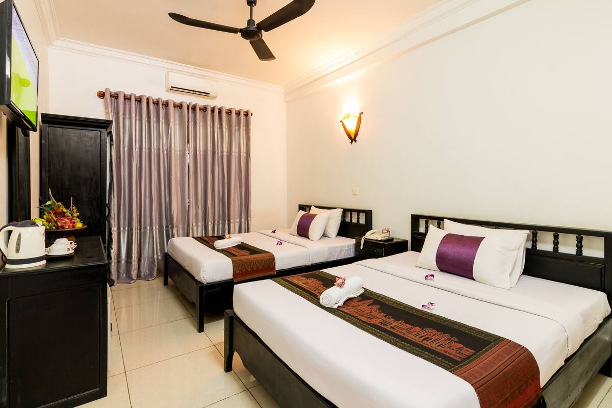 A hotel room with two beds, a ceiling fan, a TV, a coffee maker, and a fruit bowl.