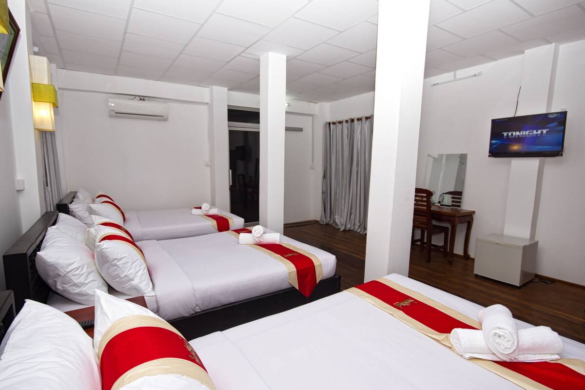 A hotel room with three beds, a TV, and a desk.