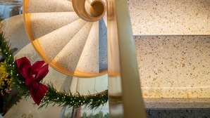 Una escalera de caracol con un lazo rojo decorativo y follaje, que conduce a un piso superior.