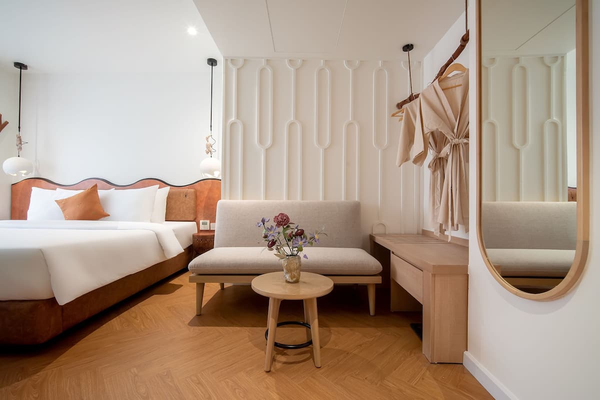 A modern hotel room with a large bed, a sofa, a small table with a vase, and a mirror.