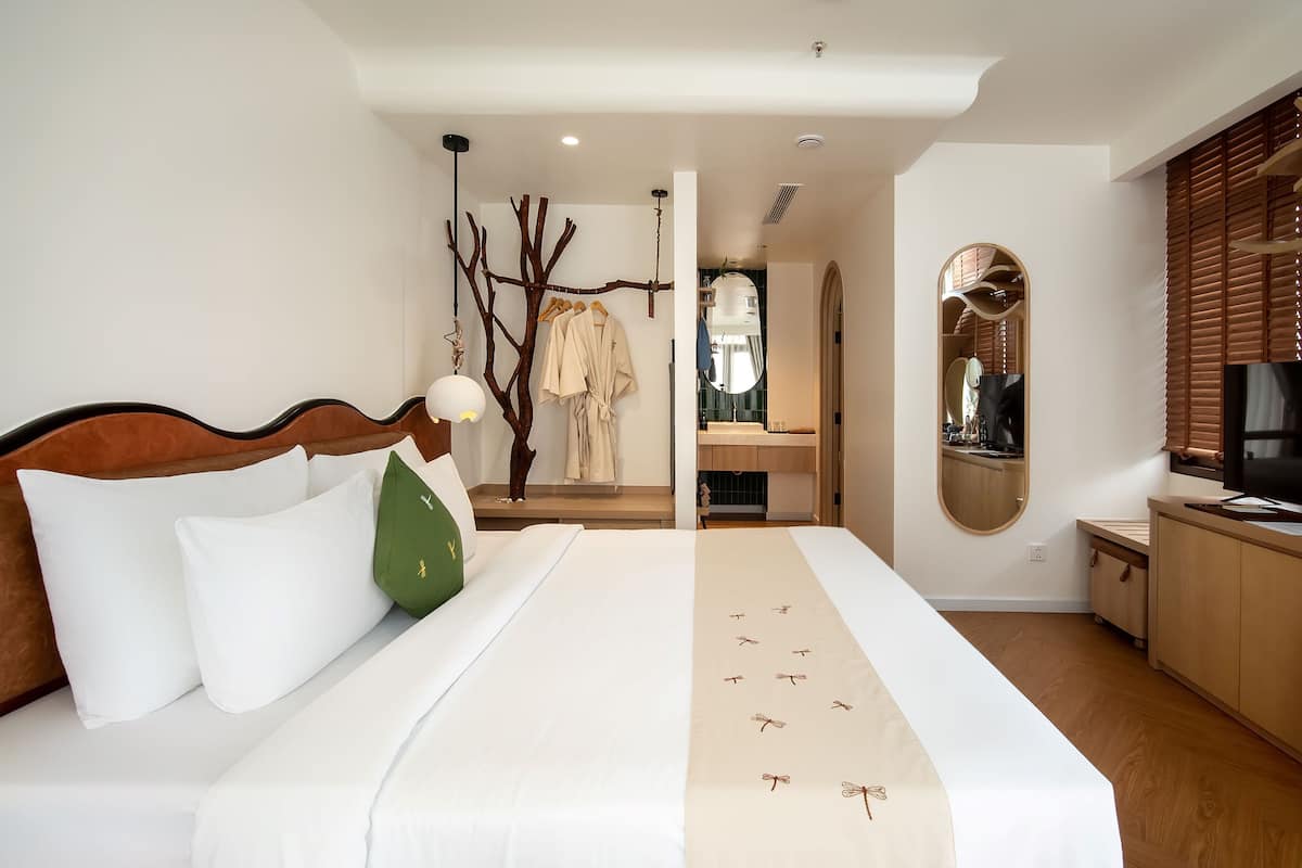 A bedroom with a large bed, a wooden headboard, a hanging branch decoration, a mirror, and a television.