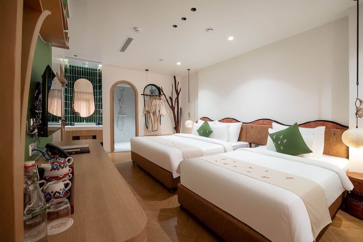 A hotel room with two beds, a wooden desk, and a mirror.