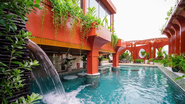 A pool area with a waterfall feature, surrounded by red architecture and greenery. - Me Saigon Boutique Hotel (Ho Chi Minh City)