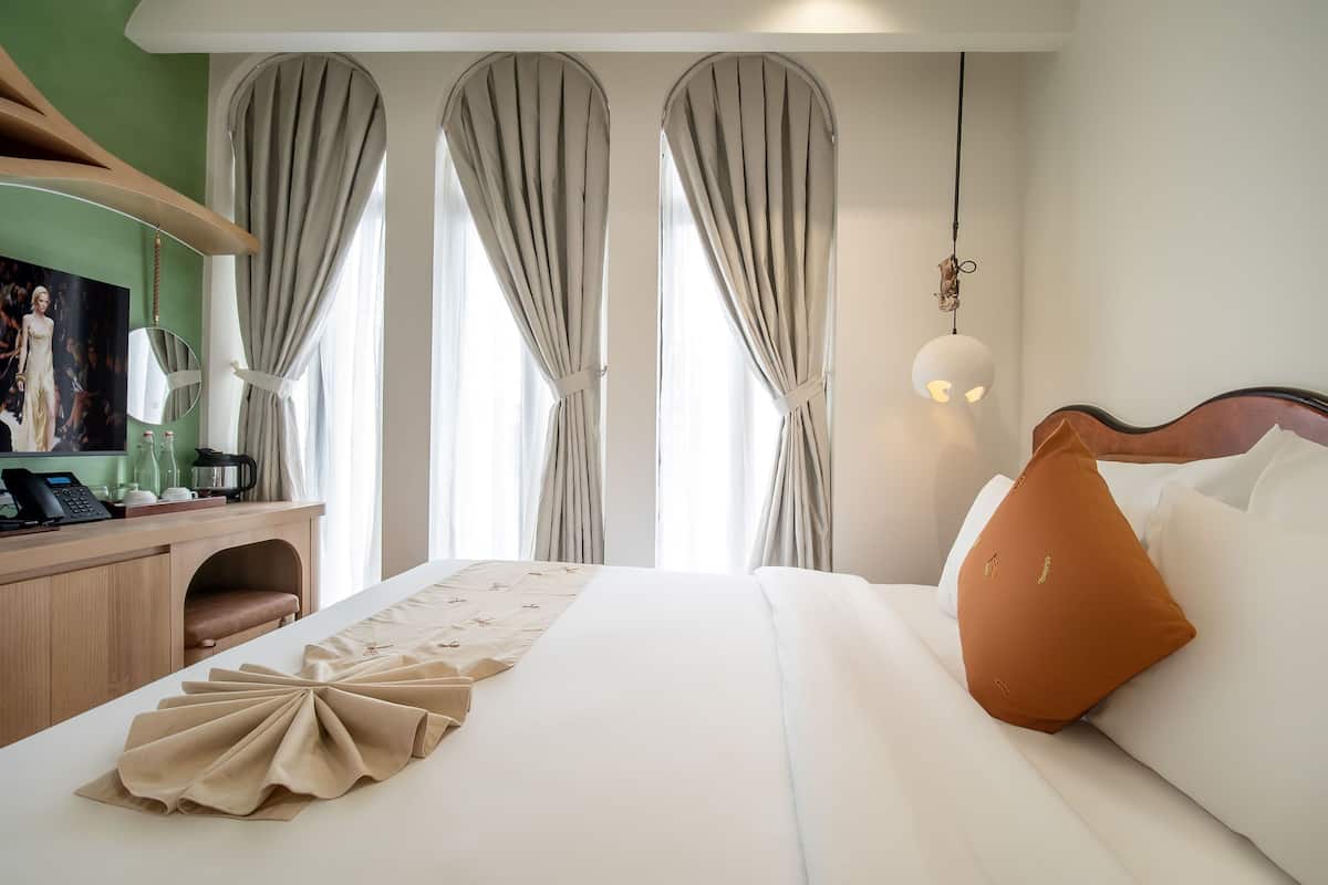 A hotel room with a large bed, a desk with a telephone, and a view of the outside through curtains.