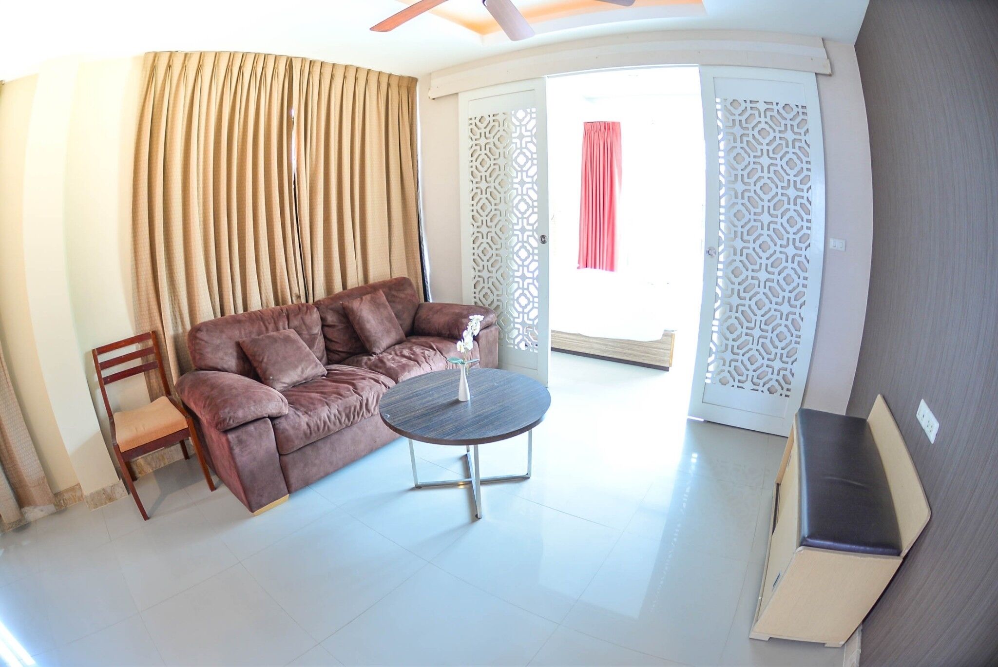 A living room with a brown sofa, a wooden chair, a small round table, and a decorative white partition.