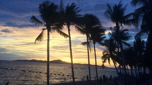A beach scene with palm trees and a sunset. - Tamnak Villa (Pattaya)