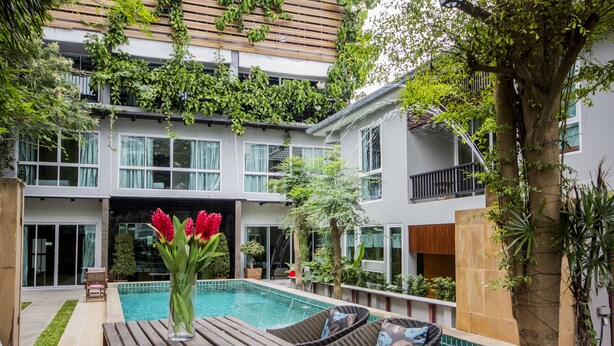 A modern two-story building with a swimming pool, outdoor seating, and lush greenery. - Tamnak Villa (Pattaya)