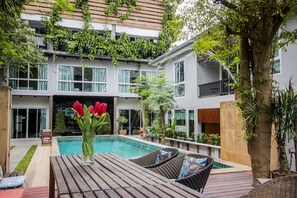 Un edificio moderno de dos pisos con piscina, mobiliario exterior y abundante vegetación.
